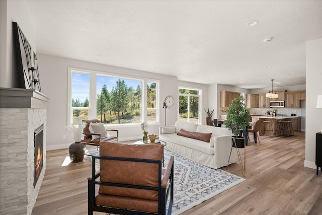 living room with recessed lighting, baseboards, a glass covered fireplace, and light wood finished floors