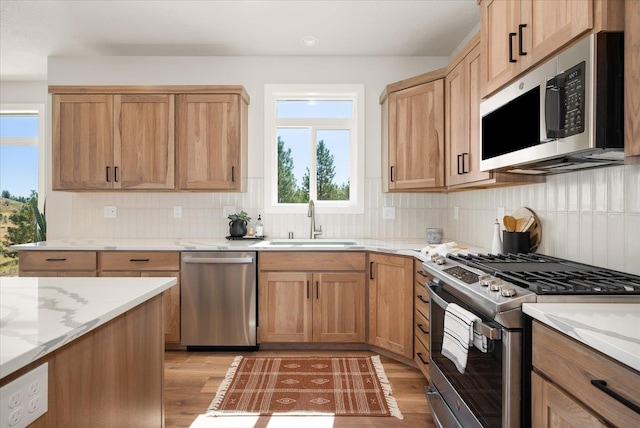 kitchen with appliances with stainless steel finishes, tasteful backsplash, a sink, and light wood-style floors