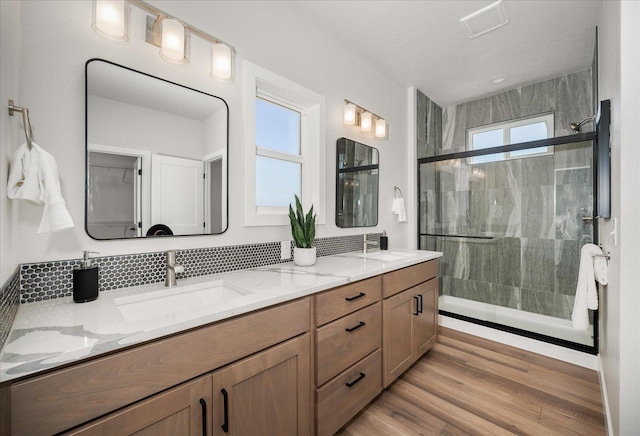 bathroom featuring double vanity, a shower stall, a sink, and wood finished floors