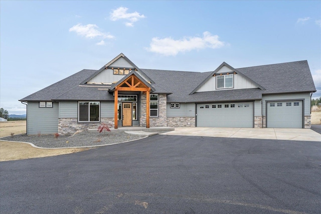 view of front of house with board and batten siding, roof with shingles, driveway, and stone siding