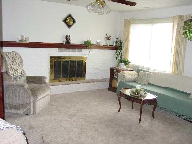living room featuring carpet flooring, a ceiling fan, and a glass covered fireplace
