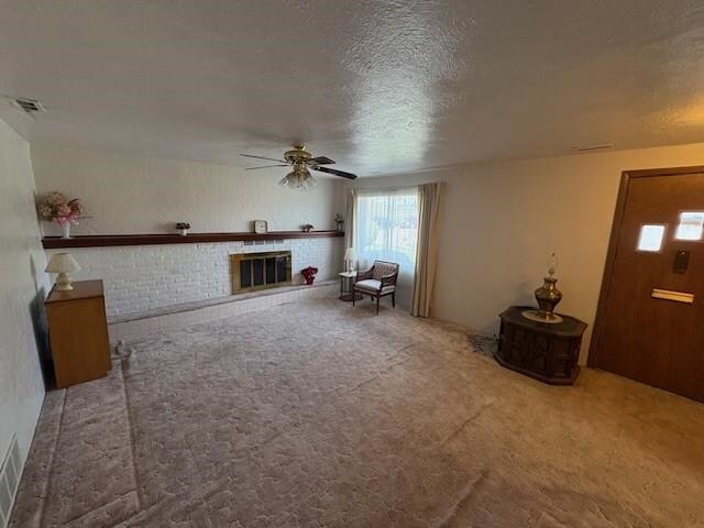 carpeted living area featuring a textured ceiling, ceiling fan, visible vents, and a fireplace
