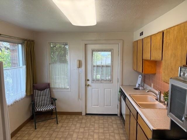 kitchen featuring light countertops, brown cabinets, a sink, and a wealth of natural light