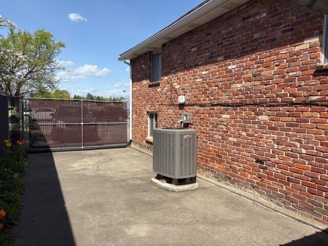view of side of property with fence, a gate, cooling unit, and brick siding