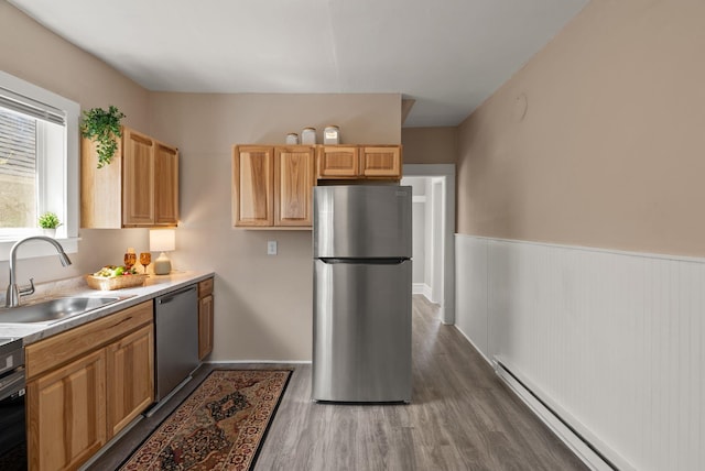 kitchen with appliances with stainless steel finishes, baseboard heating, a sink, a wainscoted wall, and dark wood-type flooring