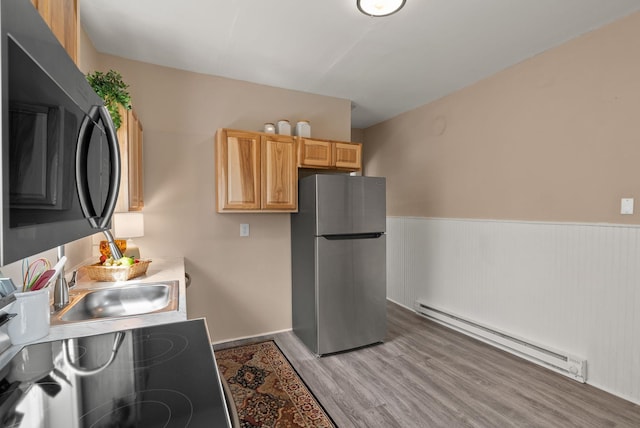 kitchen with freestanding refrigerator, wainscoting, light brown cabinets, a baseboard heating unit, and light wood finished floors