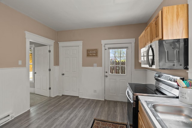 kitchen with a sink, appliances with stainless steel finishes, wood finished floors, and baseboard heating