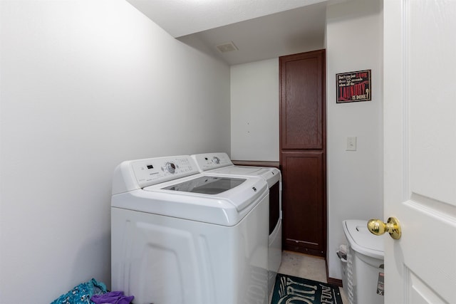 clothes washing area with separate washer and dryer, cabinet space, and visible vents