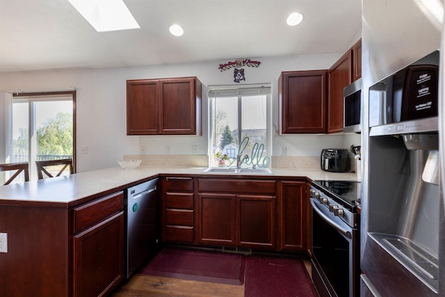 kitchen with a skylight, appliances with stainless steel finishes, a sink, light countertops, and a peninsula