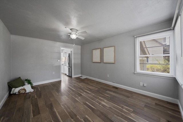 empty room with baseboards, dark wood finished floors, ceiling fan, and visible vents