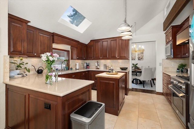 kitchen featuring appliances with stainless steel finishes, a sink, decorative light fixtures, backsplash, and lofted ceiling with skylight