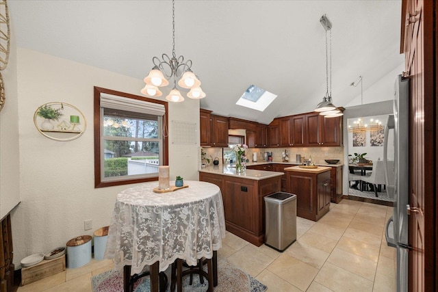 kitchen featuring an inviting chandelier, light countertops, lofted ceiling with skylight, and freestanding refrigerator