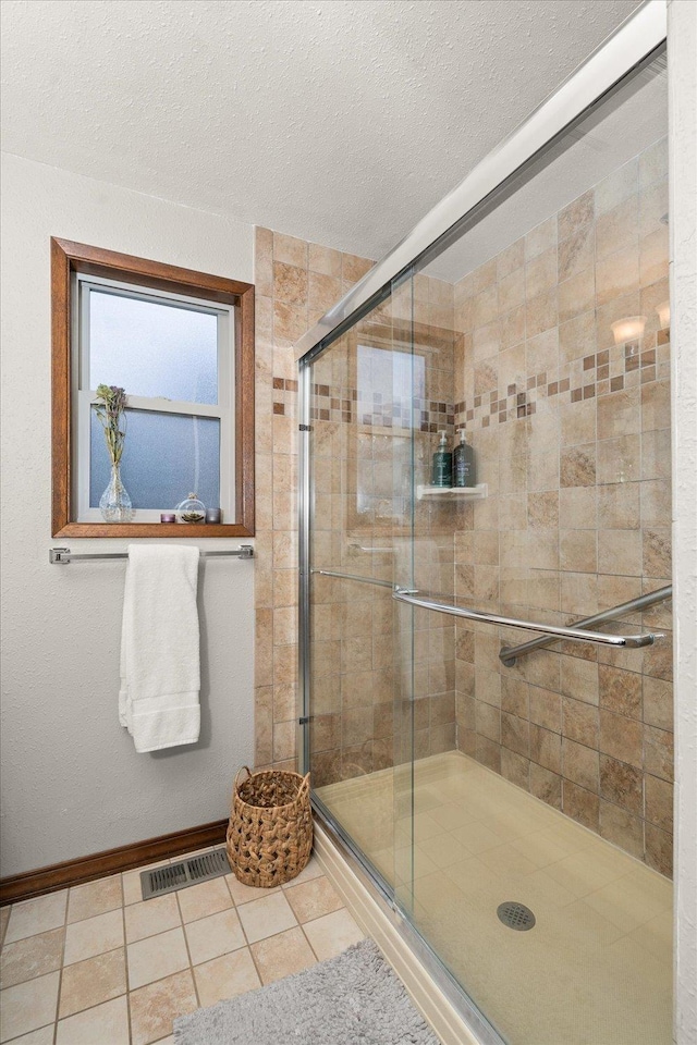 bathroom with a textured ceiling, visible vents, tile patterned flooring, a stall shower, and baseboards
