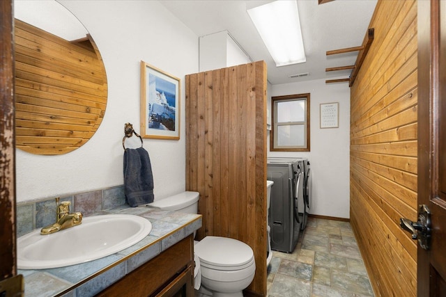 bathroom with visible vents, wood walls, toilet, stone finish floor, and independent washer and dryer