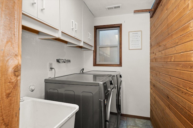 clothes washing area featuring washing machine and clothes dryer, visible vents, cabinet space, a sink, and wooden walls