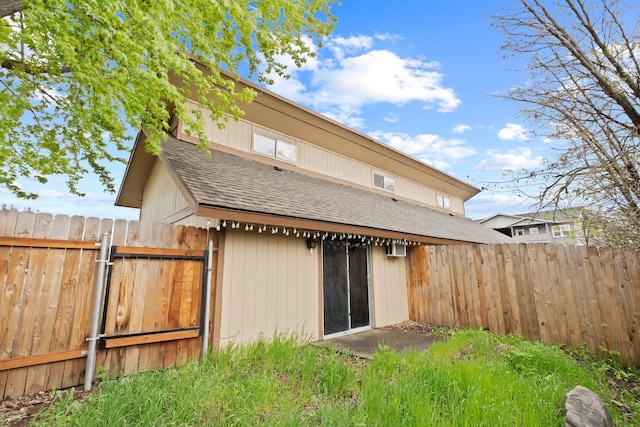 rear view of property with a shingled roof, fence, and a gate