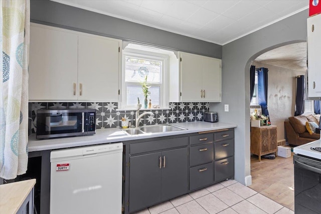 kitchen featuring crown molding, a sink, white appliances, arched walkways, and light countertops