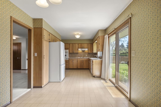 kitchen with a sink, white appliances, light countertops, wallpapered walls, and under cabinet range hood