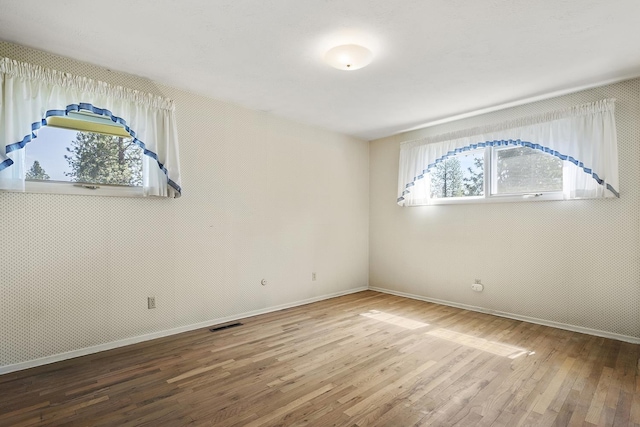 empty room featuring baseboards, wood finished floors, and visible vents