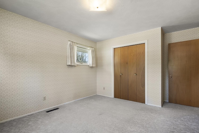 unfurnished bedroom featuring visible vents, a closet, baseboards, wallpapered walls, and carpet flooring