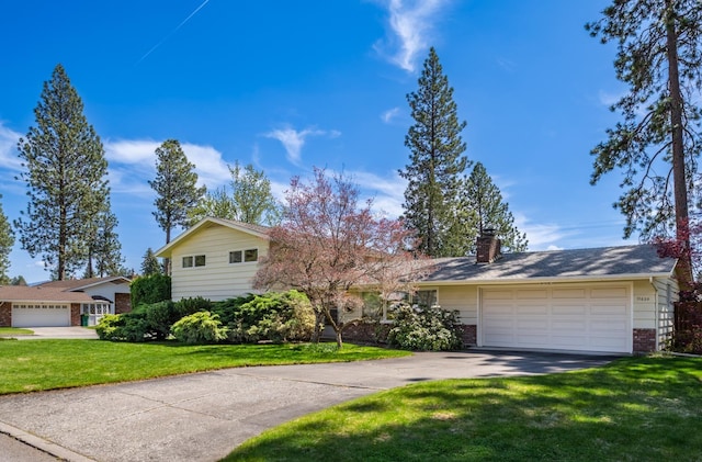 tri-level home with a front yard, a chimney, brick siding, an attached garage, and driveway