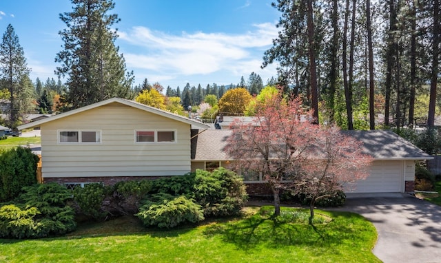 view of front of house featuring a shingled roof, an attached garage, brick siding, a front yard, and driveway
