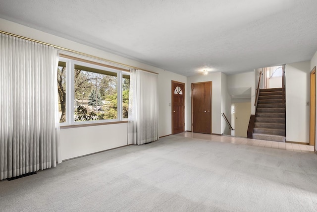 unfurnished living room featuring carpet flooring, stairs, and a textured ceiling