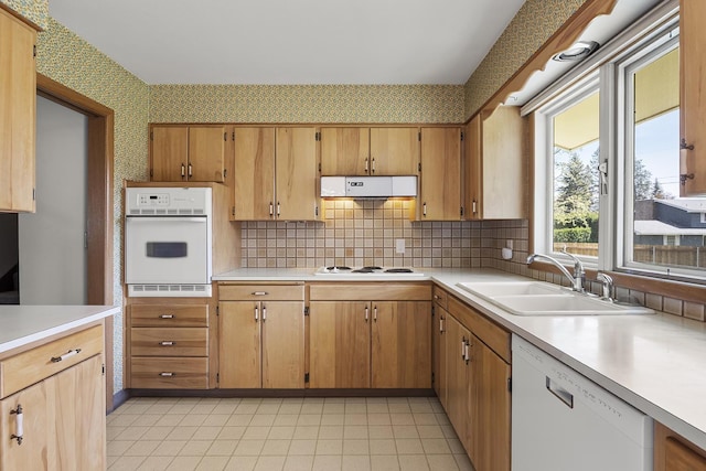 kitchen featuring backsplash, a sink, light countertops, wallpapered walls, and white appliances