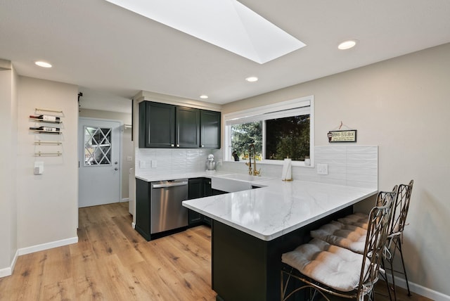 kitchen with stainless steel dishwasher, a peninsula, a kitchen breakfast bar, a sink, and a skylight