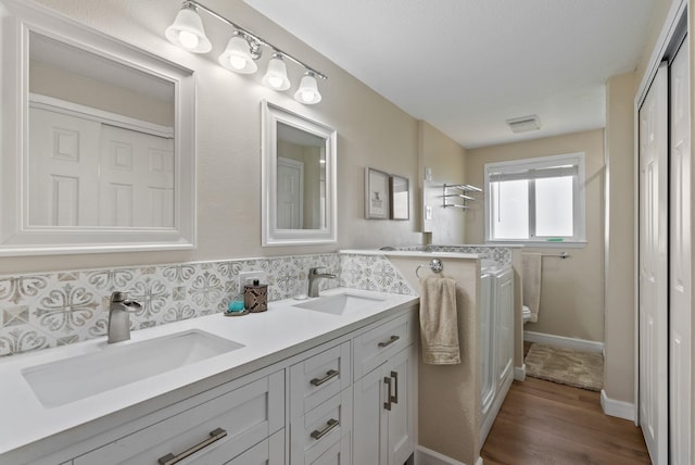 bathroom featuring visible vents, a sink, wood finished floors, and tasteful backsplash