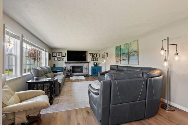 living room with a textured ceiling, baseboards, a stone fireplace, and wood finished floors