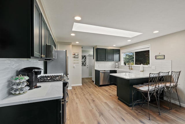 kitchen featuring a peninsula, a breakfast bar area, appliances with stainless steel finishes, backsplash, and a skylight