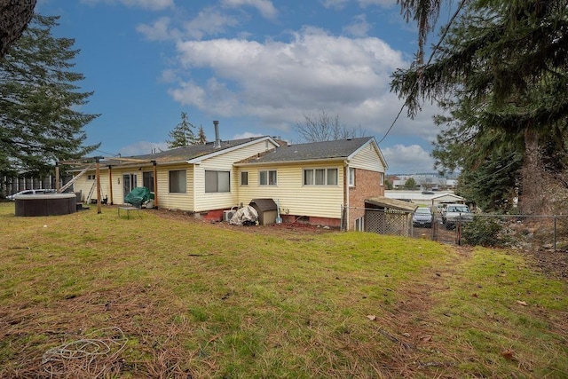 rear view of house featuring a hot tub, brick siding, a yard, and fence