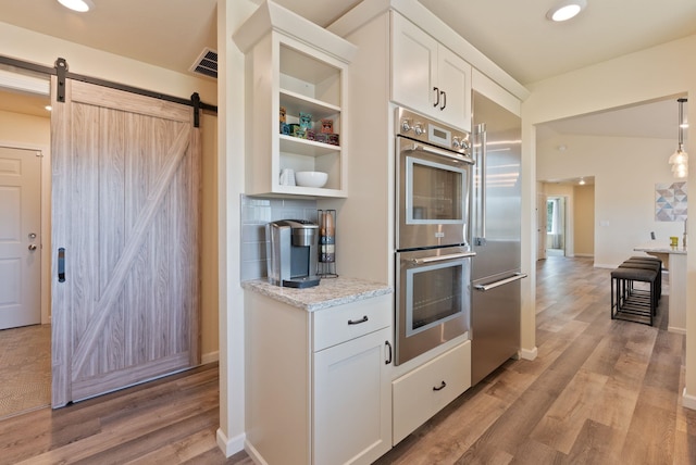 kitchen featuring white cabinetry, appliances with stainless steel finishes, a barn door, and light wood-style flooring