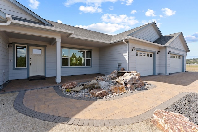 exterior space with a porch, an attached garage, driveway, and a shingled roof