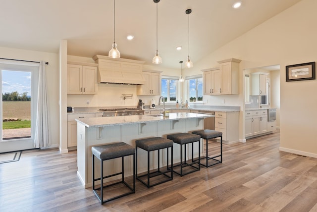 kitchen with a breakfast bar, an island with sink, custom range hood, a sink, and stainless steel gas stovetop