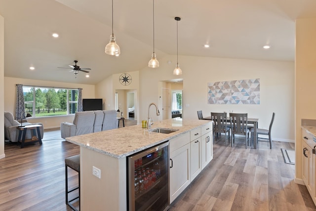 kitchen with vaulted ceiling, light wood-type flooring, a sink, wine cooler, and a breakfast bar