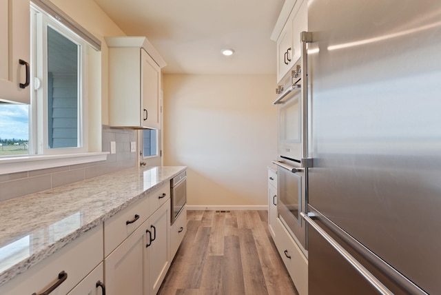 kitchen with light stone countertops, white cabinetry, tasteful backsplash, light wood-style flooring, and stainless steel appliances