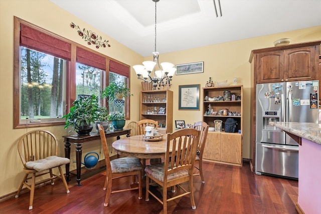 dining area featuring a raised ceiling, dark wood-type flooring, and a notable chandelier
