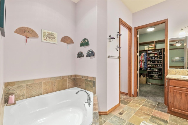 full bath featuring a walk in closet, vanity, baseboards, stone finish flooring, and a garden tub
