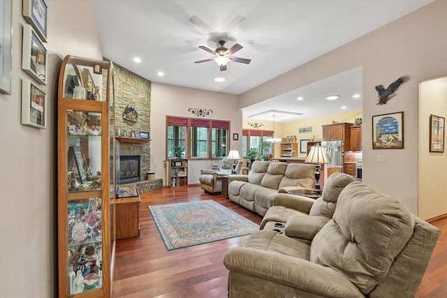 living room with a stone fireplace, recessed lighting, ceiling fan with notable chandelier, and wood finished floors