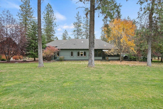 back of house featuring roof with shingles and a yard