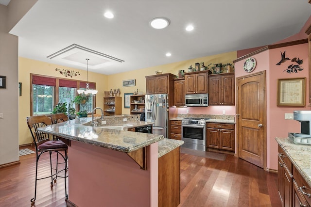 kitchen with dark wood-style flooring, light stone counters, a sink, stainless steel appliances, and a kitchen bar