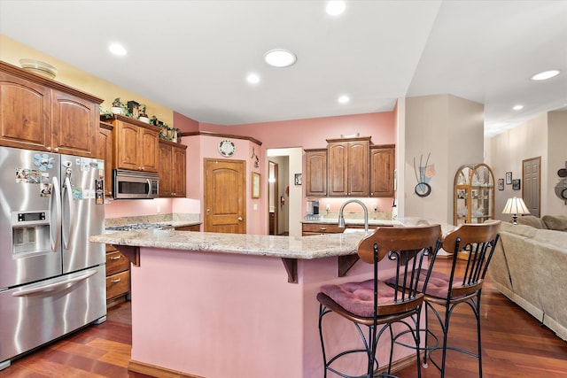kitchen featuring light stone counters, dark wood-style flooring, a breakfast bar, and stainless steel appliances