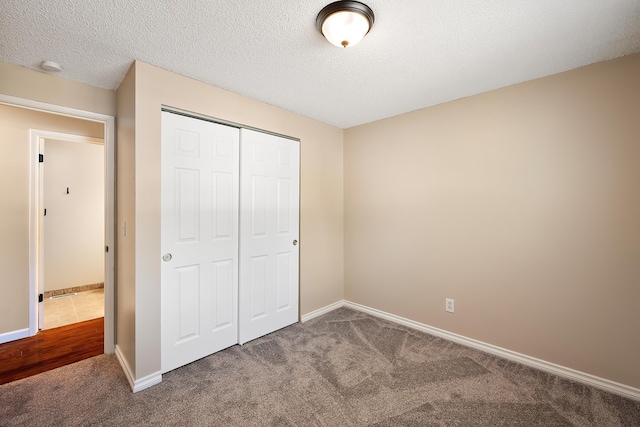 unfurnished bedroom with carpet floors, a textured ceiling, baseboards, and a closet