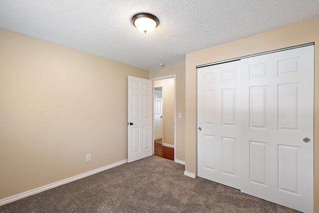 unfurnished bedroom with baseboards, a textured ceiling, dark carpet, and a closet