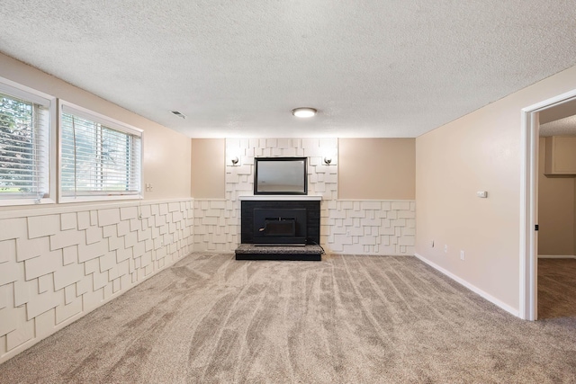 unfurnished living room featuring carpet floors, a textured ceiling, wainscoting, and a fireplace