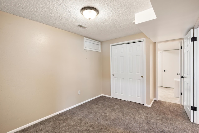 unfurnished bedroom with a textured ceiling, visible vents, baseboards, a closet, and dark carpet