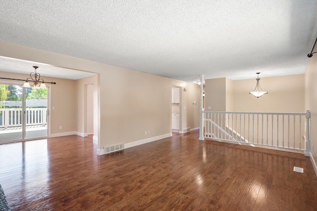 empty room featuring visible vents, an inviting chandelier, wood finished floors, baseboards, and a textured ceiling