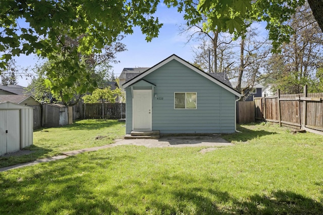 back of house with a fenced backyard, an outbuilding, a yard, and roof with shingles